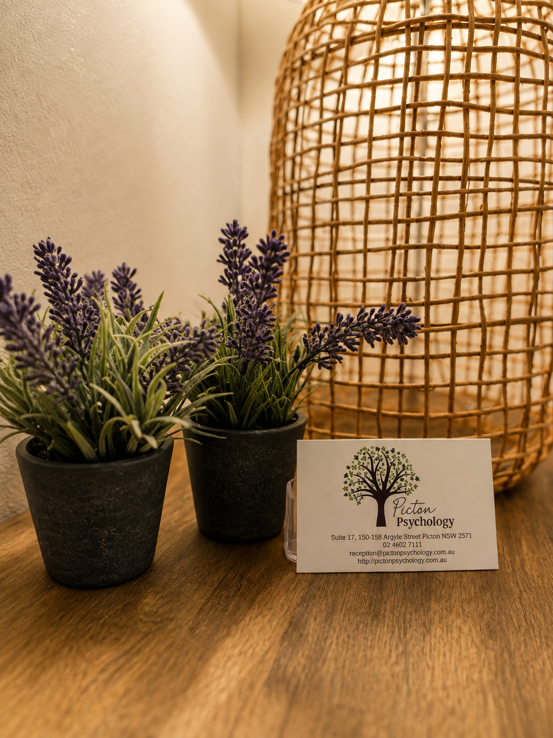 A Picton Psychology business card resting beside lavender plants and a rattan lamp